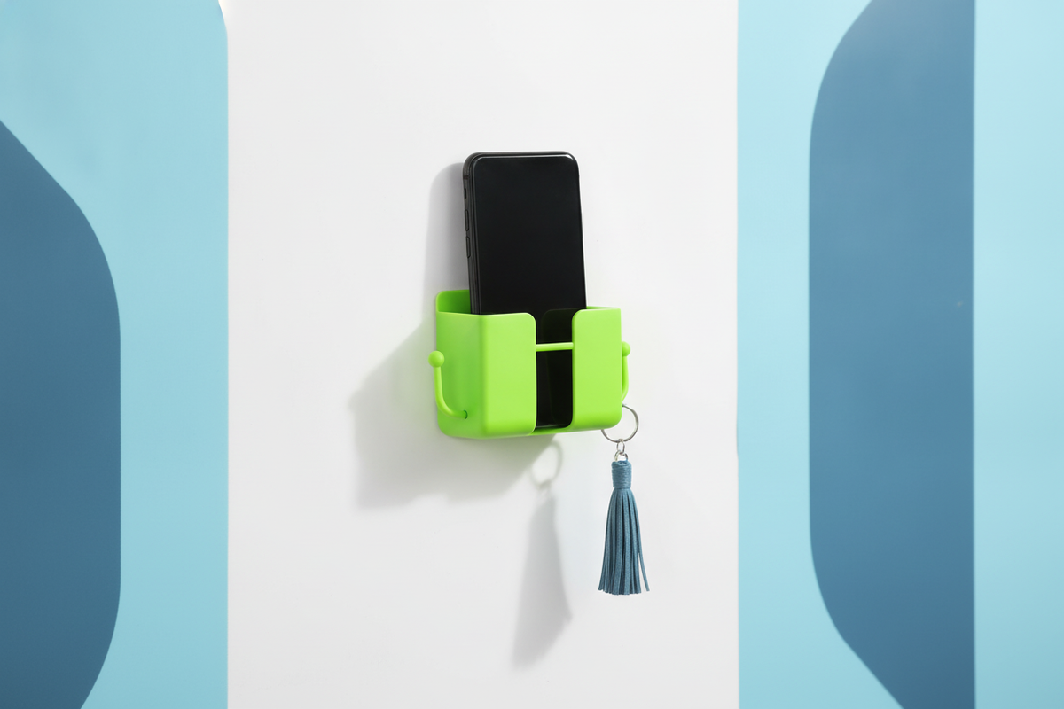 Neon green wall-mount mobile stand with hook, holding a smartphone on a bright white wall in a modern Indian home.